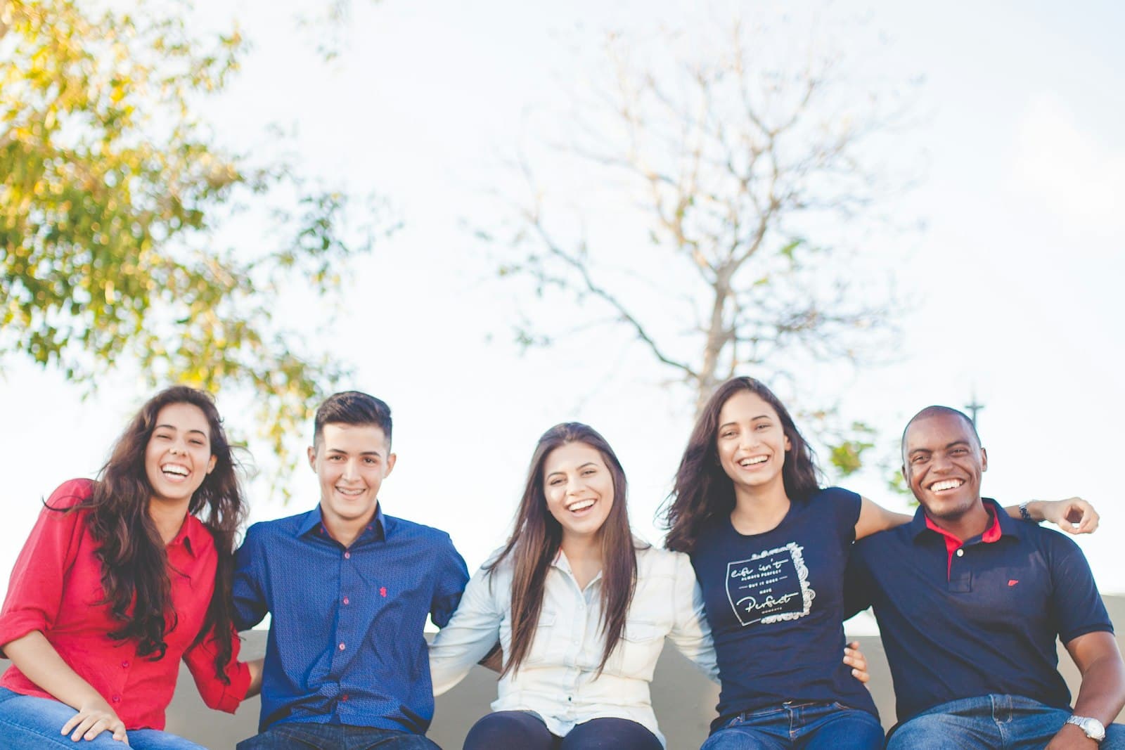 Five people sitting side by side outdoors and smiling.